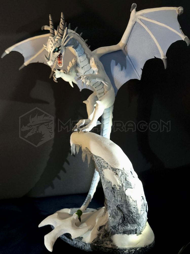 A modeled figurine of a white dragon sitting on a mountain ledge. 3/4 frontal view with a tri-bladed tail clearly visible.