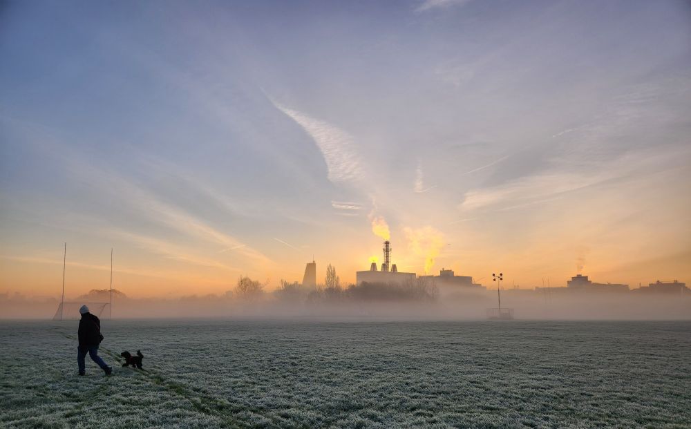 Frosty morning image of Wormwood Scrubbs, parkland in London. You can see frosted grass, a low rising mist, and the sun rising behind an industrial building