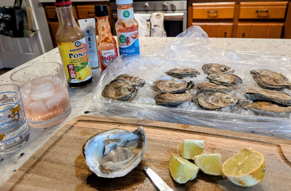On a kitchen counter are oysters, cutting board, and various sauces. 