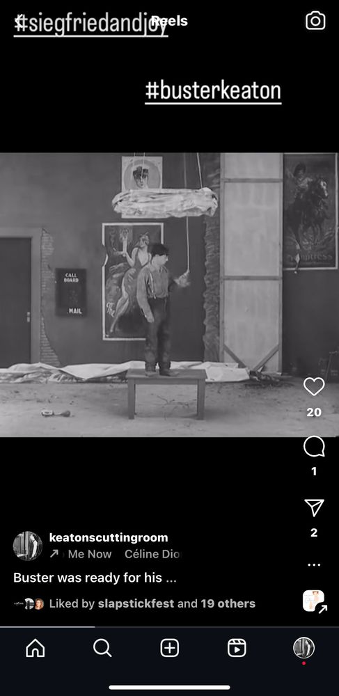 A screenshot of an Instagram reel showing a black and white frame of Buster Keaton in ‘Steamboat Bill Jr’ (1928, filmed 1927). Buster is standing on a small table in a deserted theatre about to pull a rope that will make him disappear. The Instagram text shows that the music playing is ‘All Coming Back To Me Now’ by Céline Dion. The hashtags read #busterkeaton and #siegfriedandjoy