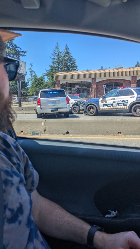 A silver hatch back with front end damage surrounded by two Saanich Police vehicles. 