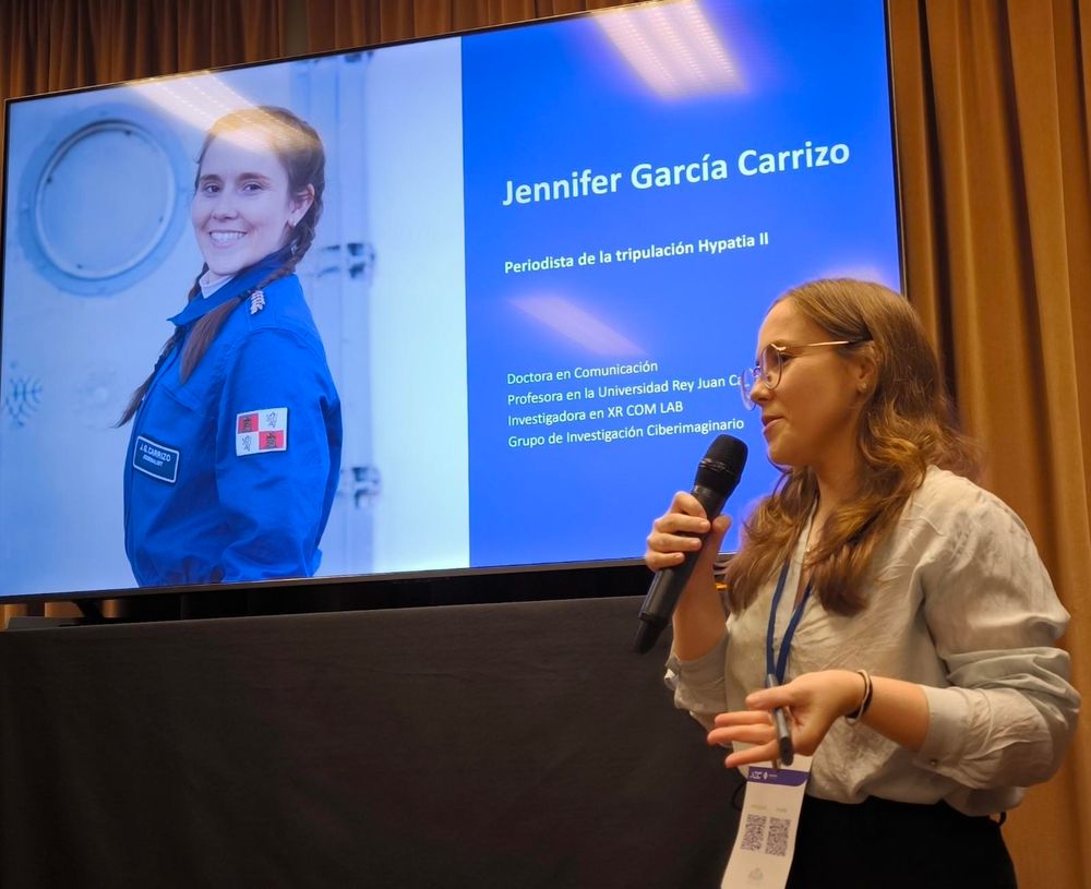 Una astronauta análoga en la foto delante de una foto suya con un mono azul.