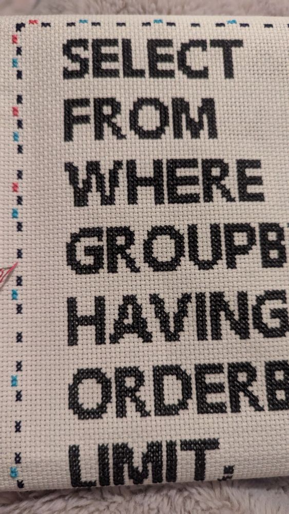 Cross stitch of SQL commands in dark grey including Select, From, Where, Groupby, Having, Order by, Limit. The cross stitch has a partially completed border with navy, bright blue, and pink.