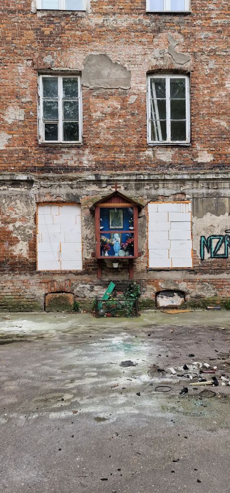Jesusfigur in einem Hof in Warschau, im Hintergrund ein sehr altes und kaputtes Haus aus der Gründerzeit. 