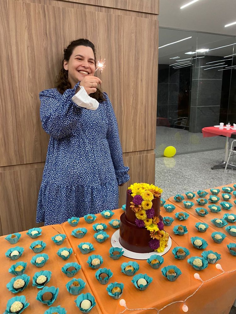 Foto de mesa de aniversário com docinhos e um bolo, aniversariante sorrindo com vela na mão