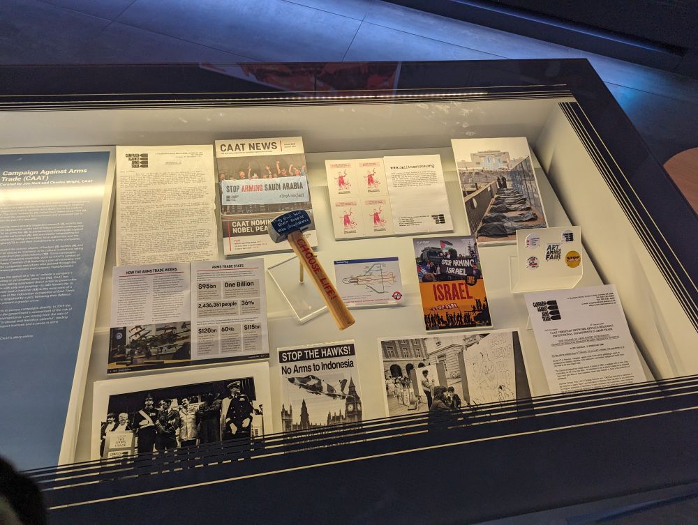 A case with various items on display from Campaign Against Arms Trade (CAAT), including a hammer and photos.
