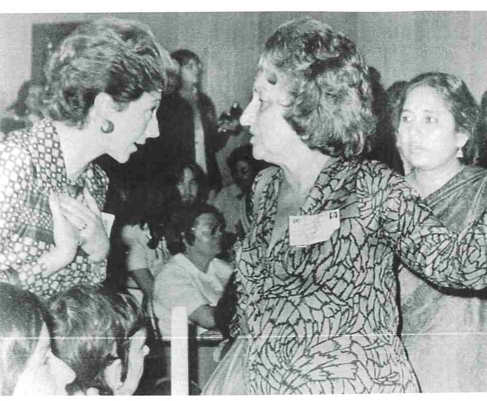 Black and white photograph of 2 women (delegates) in conversation with other women around them - Betty Friedan and another delegate of the conference. 