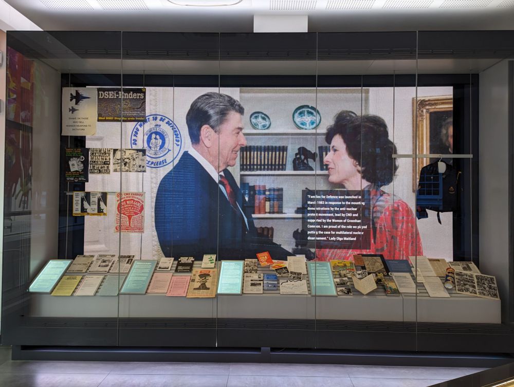 A large screen displaying a photo of two people meeting each other. One is Ronald Reagan and the other Lady Olga Maitland. Various other objects are on display.