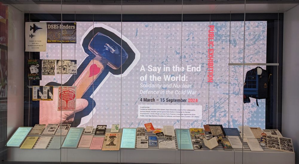 A large screen displaying a hammer and details of an exhibition. Within the casing are various items on display including a jacket.