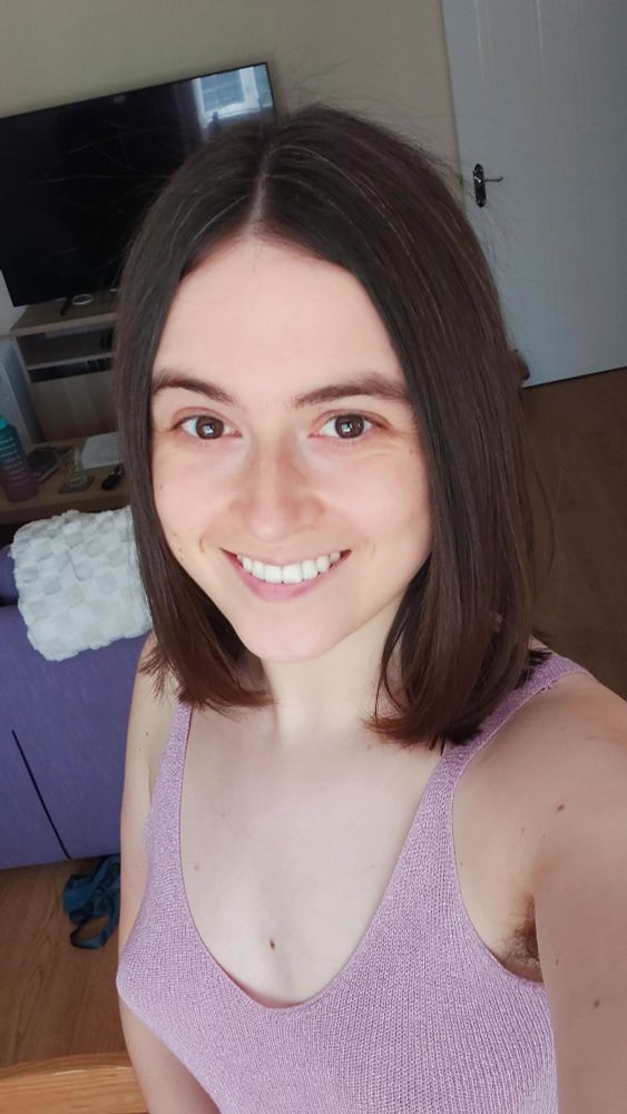 A selfie of Chloe (a white late-20s woman) in her living room with a new haircut - a shoulder length dark brown bob.