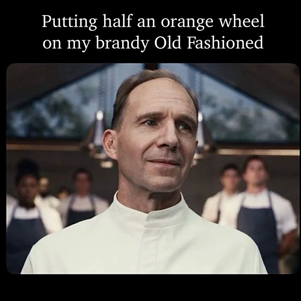 Ralph Fiennes as the imperious, self-satisfied Chef Slowik while a brigade of cooks stand at attention in the background from the film The Menu. Text above the image reads:

Putting half an orange wheel on my brandy Old Fashioned