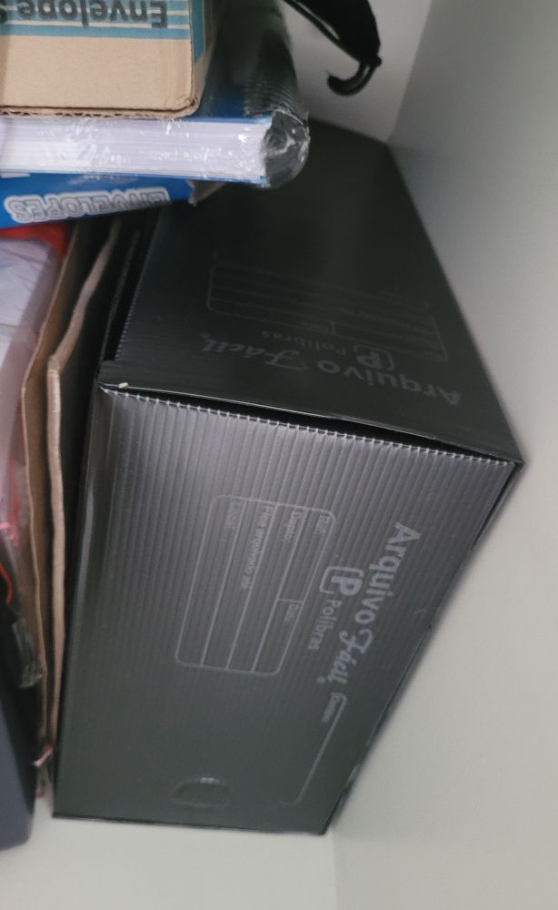 Caixa de arquivo morto preta, dentro de armário com algumas bagunças.