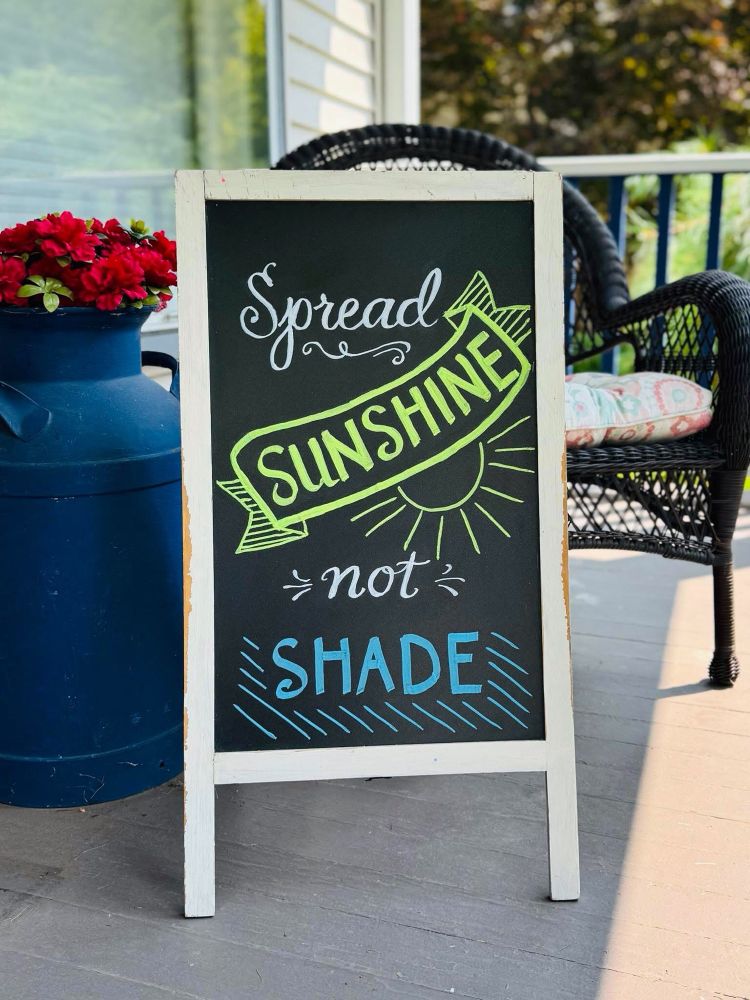 Chalkboard on a porch reads “Spread Sunshine, not Shade”