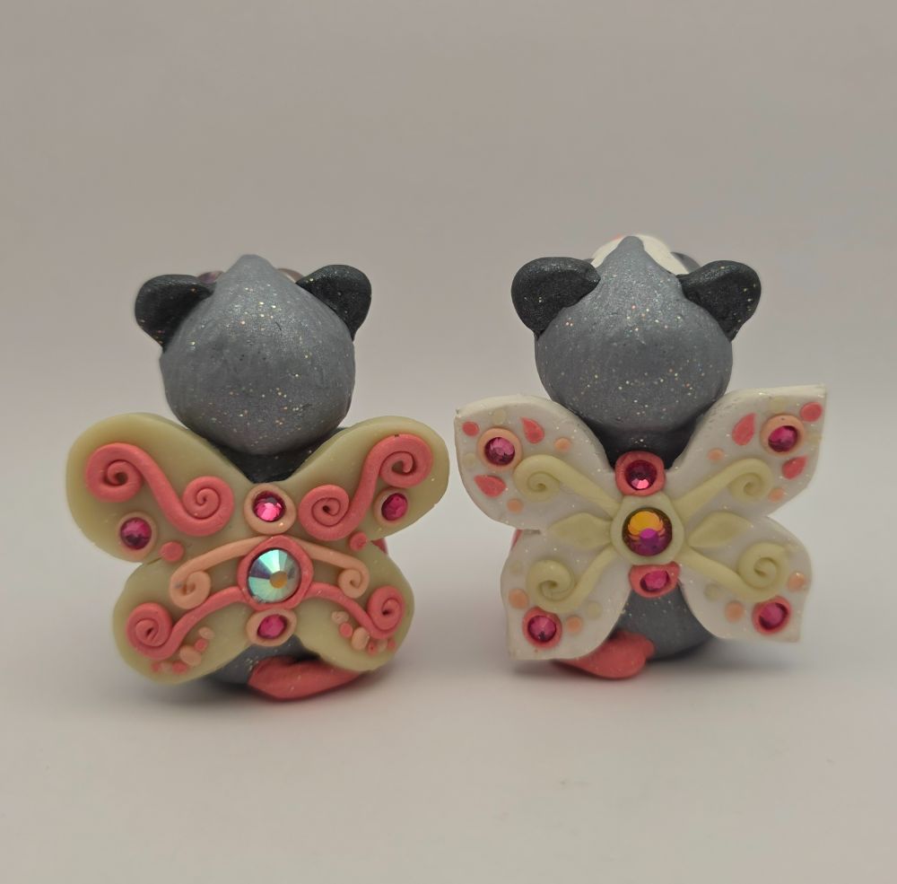 Two little fairy opossums from behind, showing off their swirly wings decorated with rhinestones and swirls. 