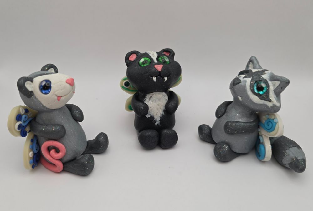 Three fairy creatures: an opossum, a skunk, and a raccoon, each with heart shaped noses and fangs.