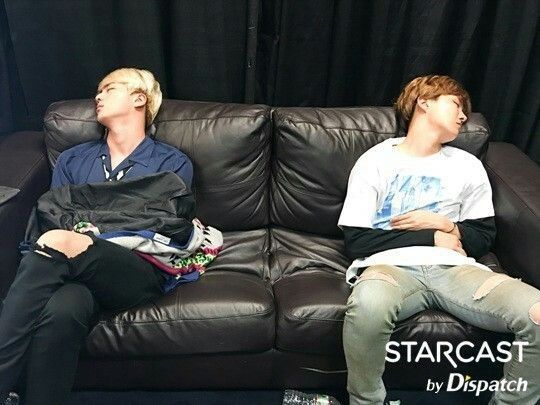 Hobi and Jin on opposite ends of a black leather couch. They are both facing opposite sides and sleeping.