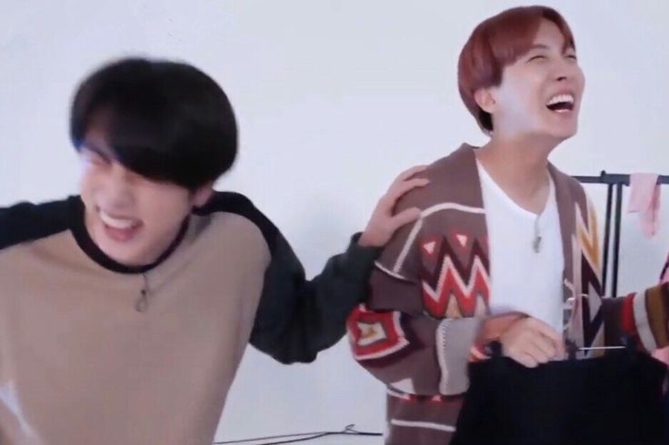 Jin and hoseok laughing. Jin is a little blurry and is resting g his gand on Hoseok's shoulder while Hoseok is laughing, holding a shirt/jacket on a hanger.