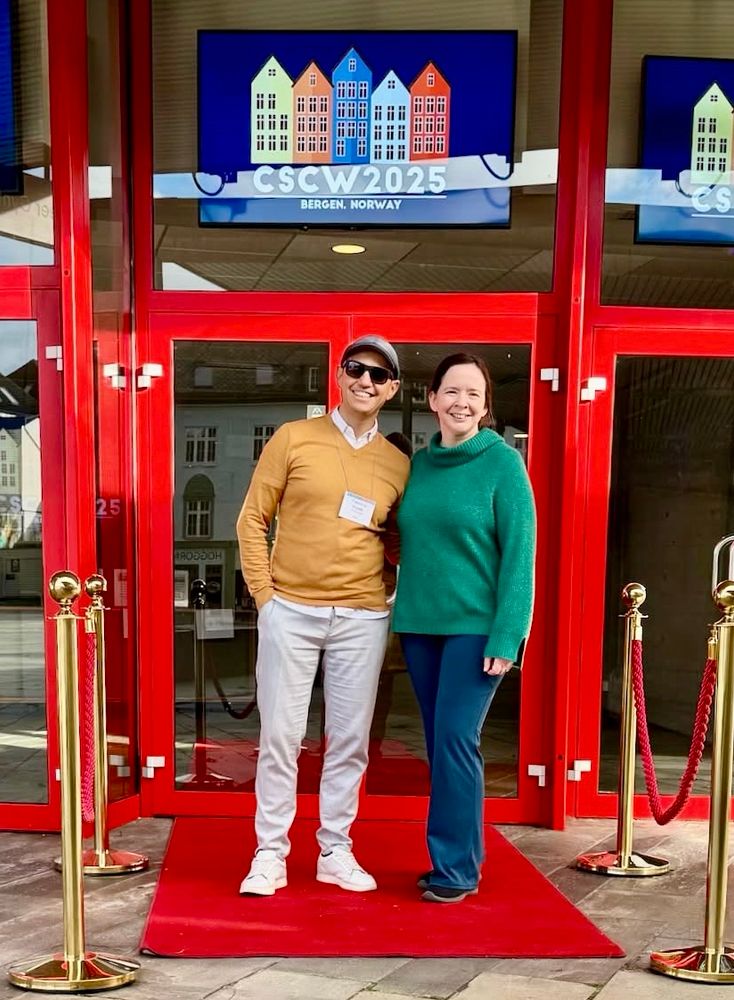 Fabiano and ajessica stand at the entrance to the Grieghallen, on a red carpet with the CSCW logo above their heads.