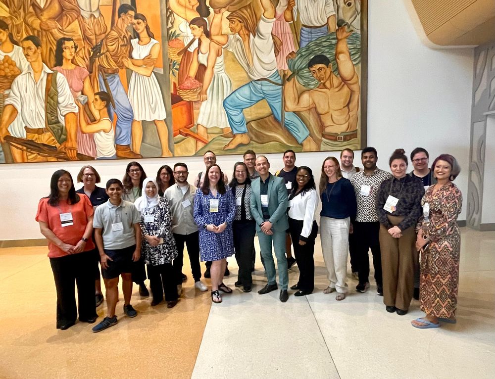 Group picture of 20 members of the 2025 CSCW organizing committee, standing in front of a large painting at the San Jose (Costa Rica) convention center.