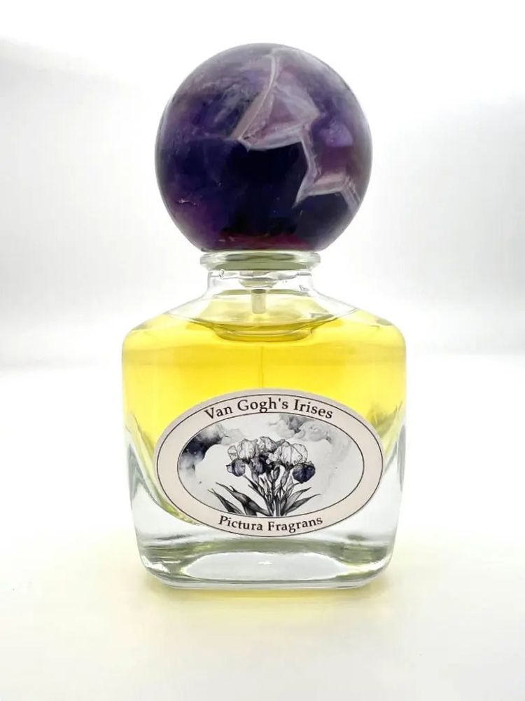 Pictura Fragrance website photo of a full bottle of Van Gogh's Irises, which is in a clear bottle with pale yellow juice and an amethyst sphere cap.