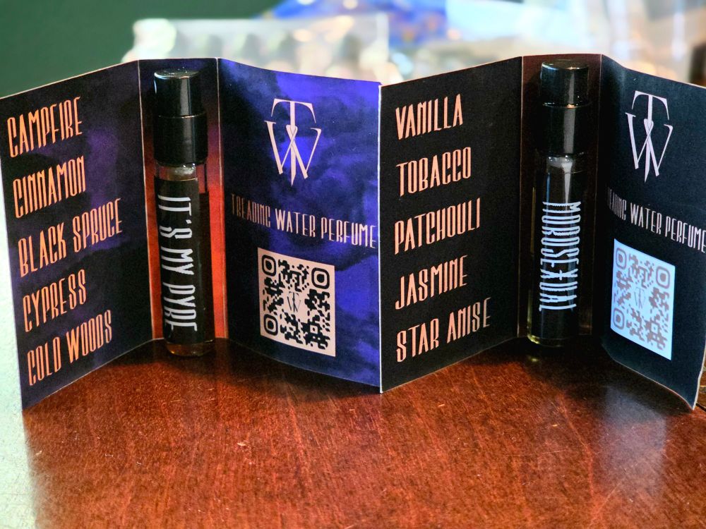 Two sample spray vials of perfume with their corresponding cards that list the notes. It's My Pyre notes: campfire, cinnamon, black spruce, cypress, cold woods. Morosexual notes: vanilla, tobacco, patchouli, jasmine, star anise.