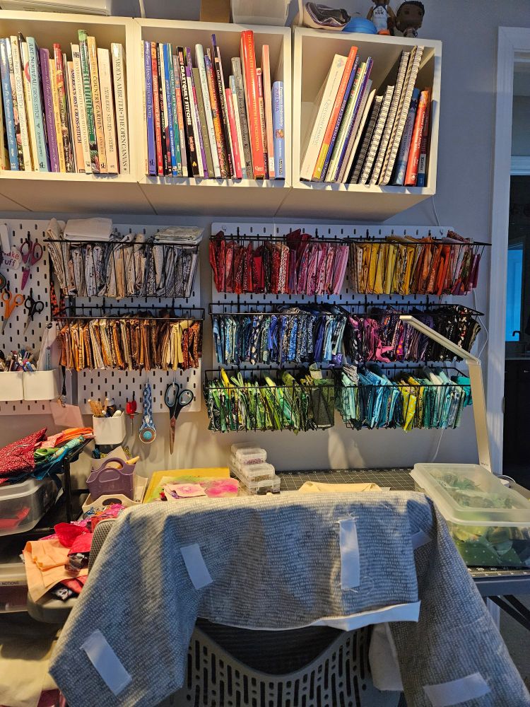 My textile art space, with baskets of fat quarters in every color on the wall 