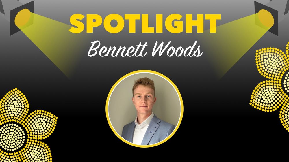 Headshot of a man wearing a light blue suit jacket and white shirt, centered under the text 'Spotlight Bennett Woods' with decorative yellow flowers.