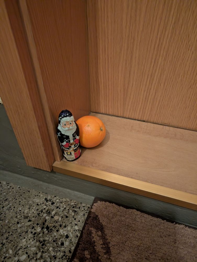 Schokoweihnachtsmann und Apfelsine auf der Schwelle einer Nachbarstür