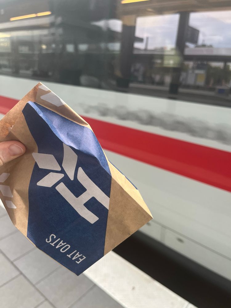 Triumphierend haltende Tüte mit was zu Essen vor einem einfahrenden Zug.