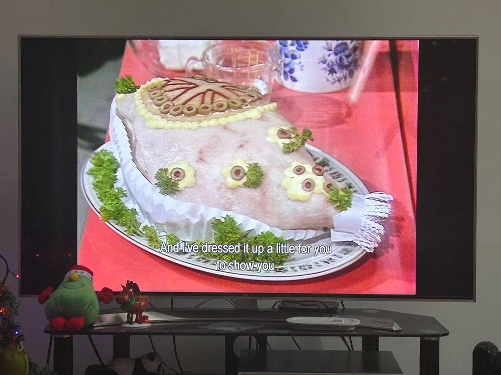 A TV screen showing some kind of ham monstrosity, which has flower shaped that look like they’re made of butter and maybe sliced olives and parsley? It is not revealed on the show what these horrors are.