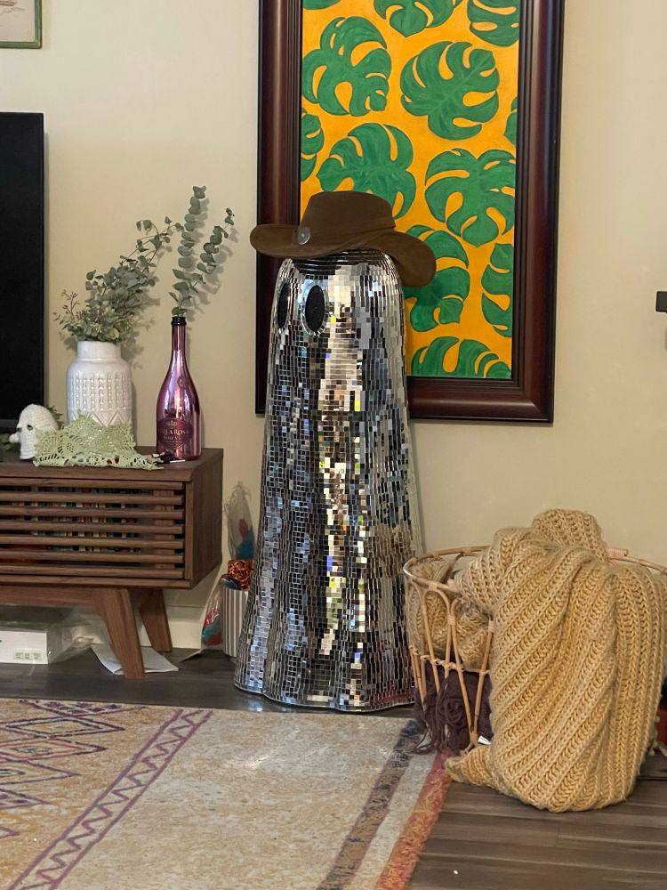 A ghost statue covered in silvery mirror tiles like a disco ball. It is wearing a cowboy hat.