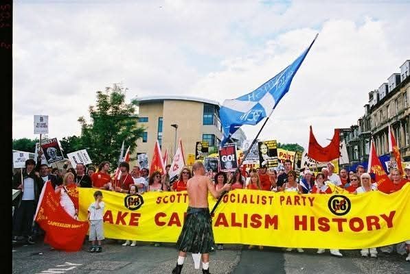 Make Capitalism History banner at the Edinburgh Make Poverty History rally. Man with kilt waves large Saltire in front of rally.