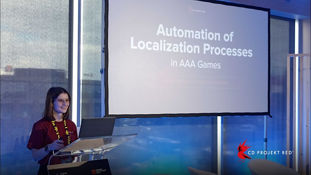 A CD Projekt Red employee smiles from behind a podium, microphone in hand. Next to her a large screen reads, “Automation of Localization Process”.