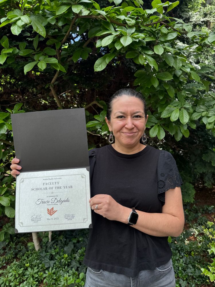 Professor Delgado holding up a Faculty Scholar of the Year award certificate 
