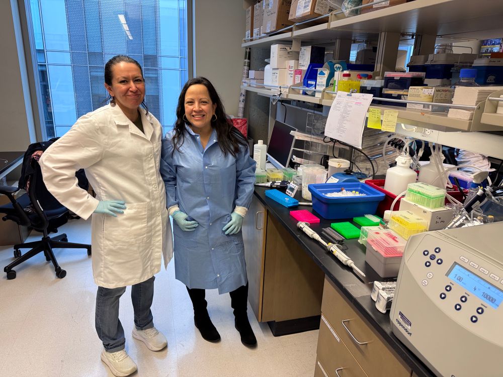 Two women scientist posing for a picture in front of a lab bench