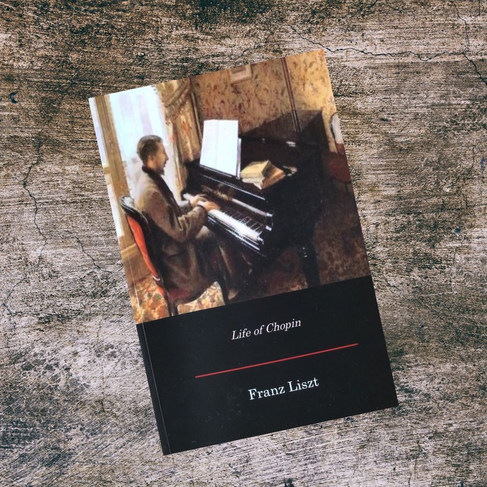 A paperback copy of "Life of Chopin" by Franz Liszt rests on a textured, weathered stone surface. The book cover features a painting of a man seated at a piano, reading sheet music in a warmly lit, wallpapered room.