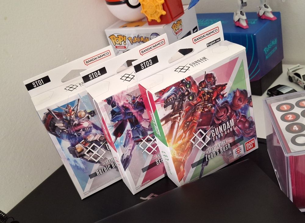 Decks de Gundam Card Game. Ao todo 3, em ordem: starter deck 01 - Heroic Beginnings, 04 - SEED Strike e 03 - Zeon's Rush