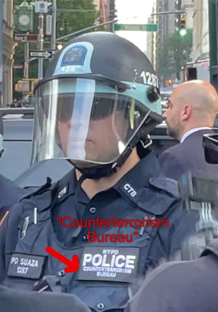 NYPD Police Officer wearing a vest that says "Counterterrorism Bureau." The officer is also wearing a helmet with a face shield.