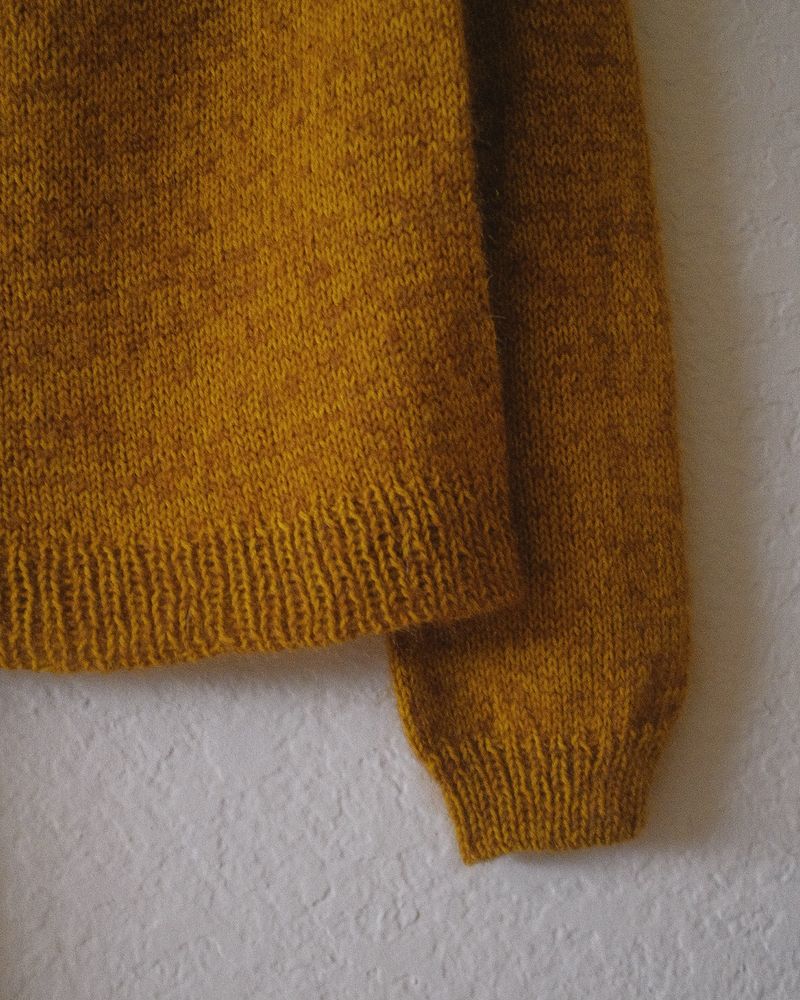 Close up of sweater on a hanger: detailing the body and arm cuff ribbing
