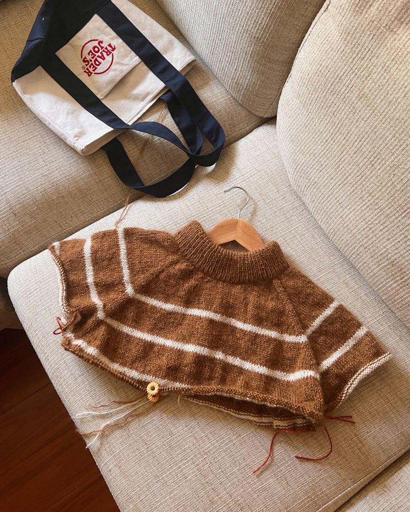 Top down photo of a half constructed knit sweater. The sweater is a warm goldenrod brown base with thin light cream stripes.