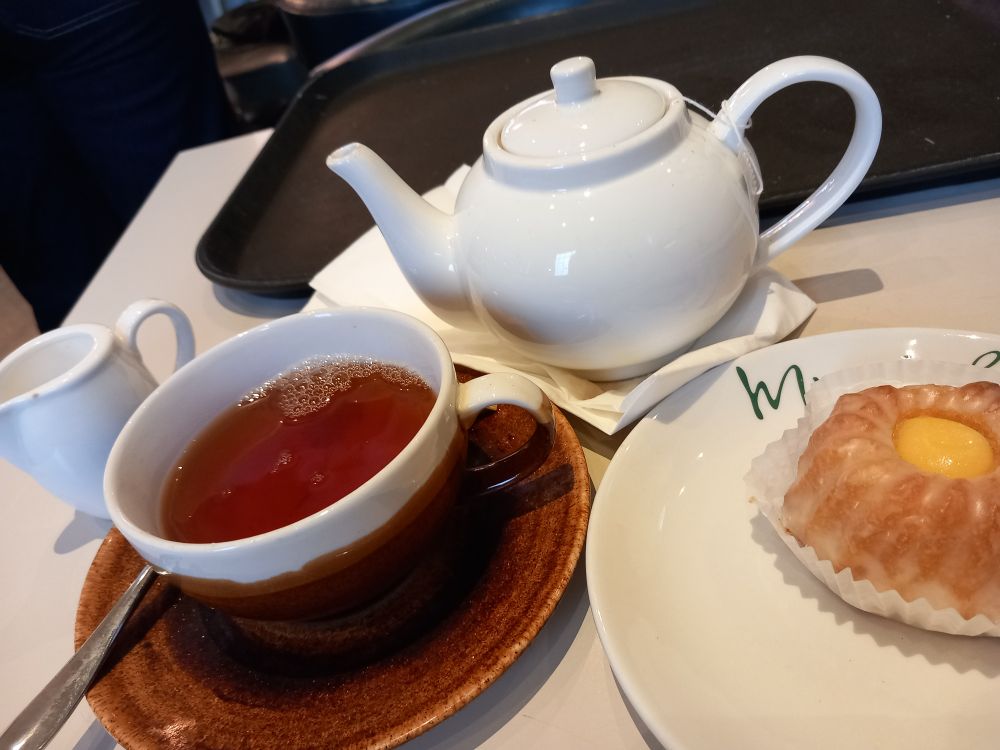 White teapot and milk jug, brown cup and saucer (cup with a white top to show it is all a set), tiny bundt cake alongside