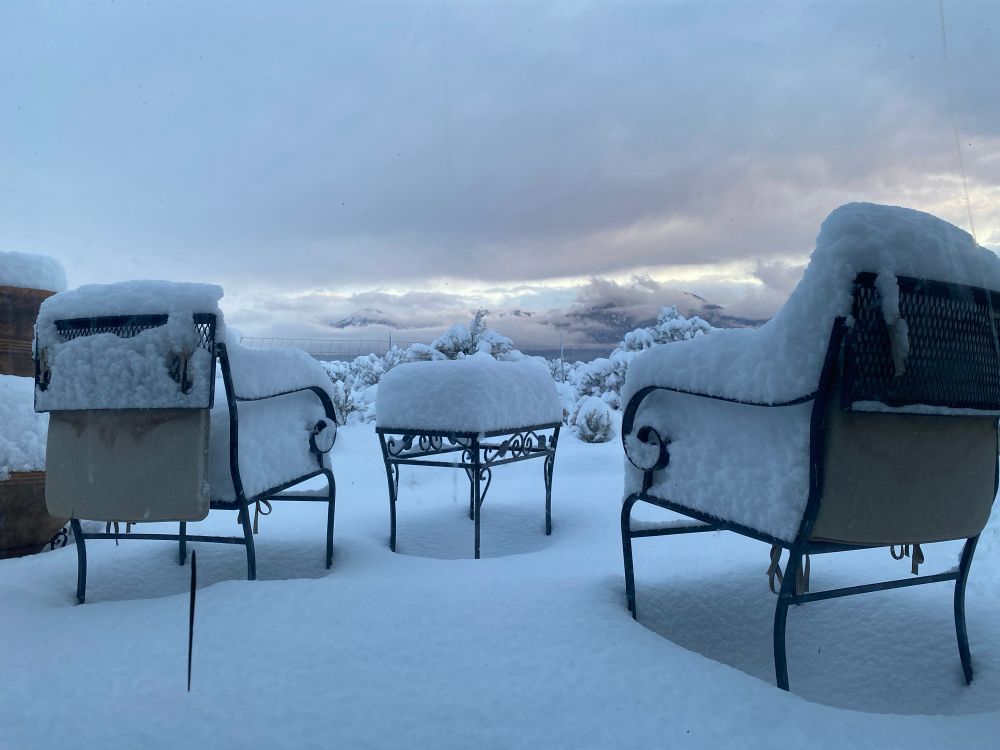 Two metals chairs and a small table sit in deep banks of snow with nearly a foot of powder piled on top. 