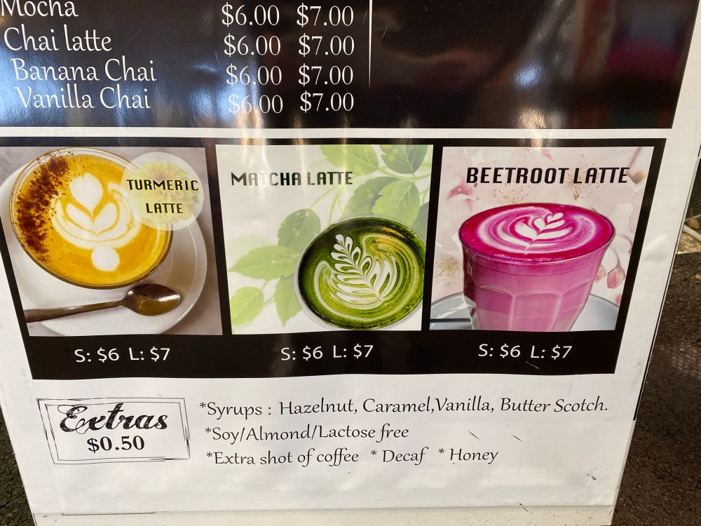 A coffee price board with pictures of three drink options: a golden turmeric latte, a green matcha latte, and a pink beetroot latte