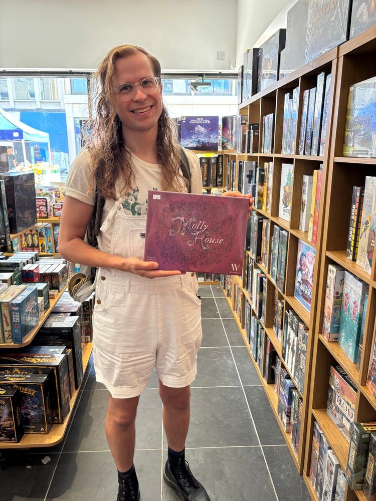 Jo Kelly (me!) holding a copy of the board game Molly House at Excelsior!, a board game shop on Bristol