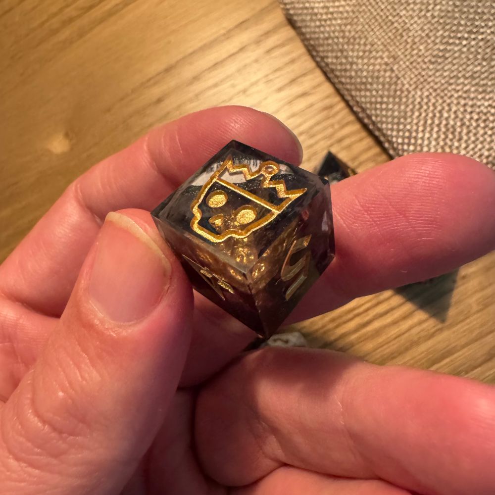 A six-sided die with an image of a skull wearing a crown on the face instead of the number 6.