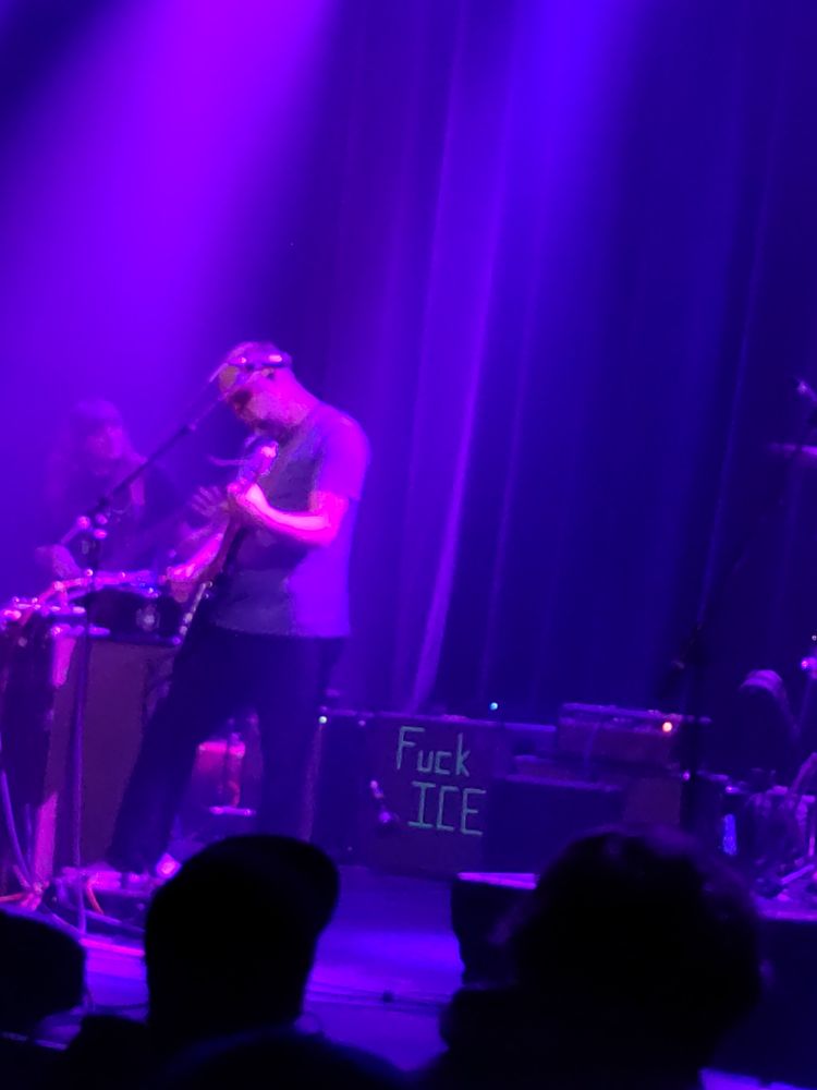 Doug Martsch plays guitar in front of an amp with the words FUCK ICE on it in green letters