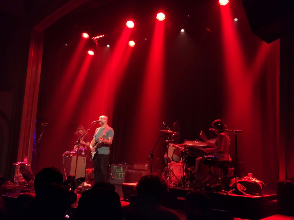 The band Built to Spill performs under red lights with the words FUCK ICE written on an amp