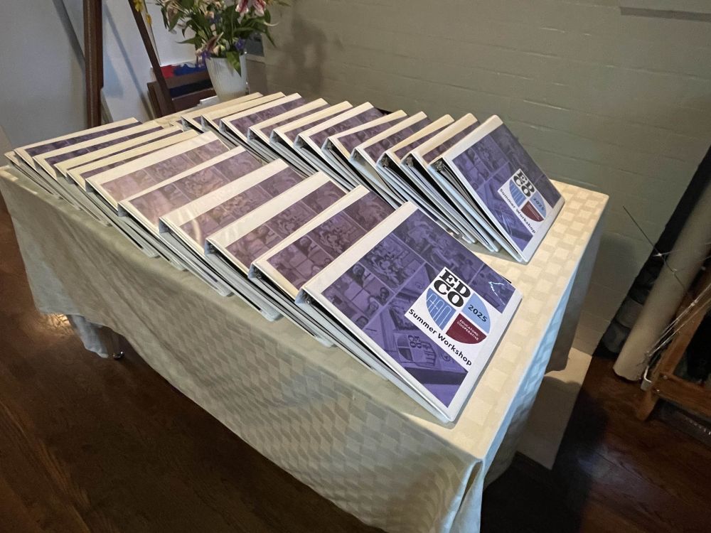 A photograph of a table stocked with EdCo Summer Workshop binders.