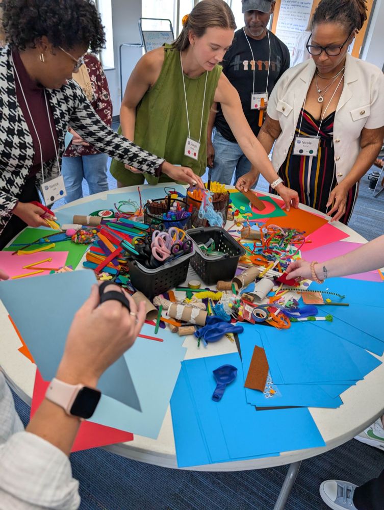 A photograph of ~7 educators approaching a table with arts and crafts supplies.