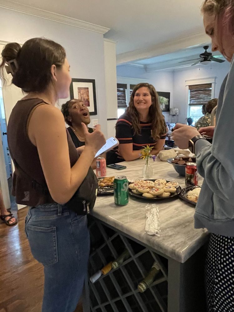 A photograph of ~4 educators socializing at a kitchen island with ~3 other educators in the background.